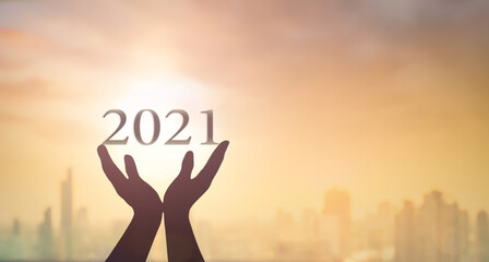 New year 2021 concept: Silhouette hands show 2021 against blurred city sunrise background