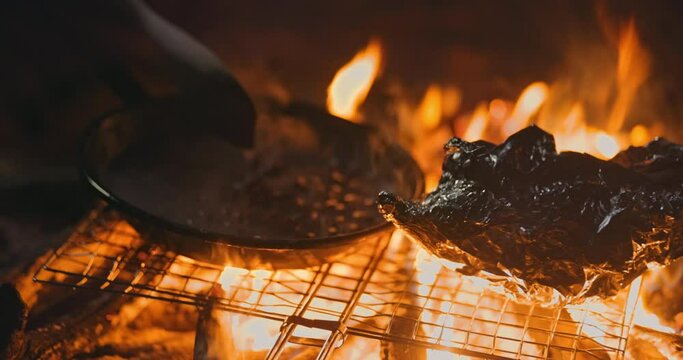 Person cooking beans and roasting food on foil at campfire