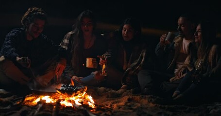 Friends cooking and drinking on beach bonfire at night