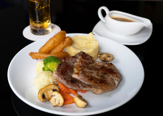 Rib eye beef steak with mashed potatoes mushrooms, onion rings. Served with pepper sauce