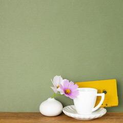 Coffee cup with common cosmos flowers and audio cassette tape on wooden table. Khaki green...