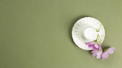 White empty mug cup with common cosmos flowers on khaki green background. top view, copy space