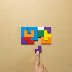 Set of color blocks puzzle pieces and hand holding last one piece on brown background. Creative...