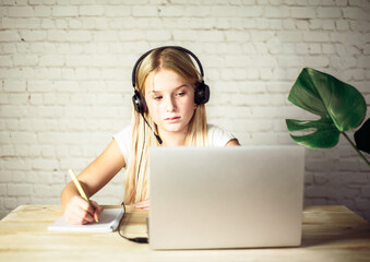 Children home schooling, teenage girl in headphones studying online at home, e-learning concept