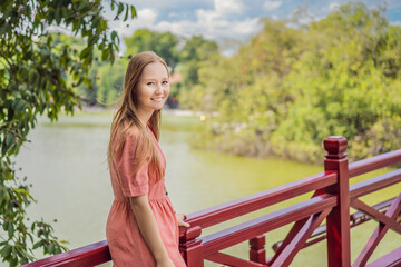 Caucasian woman traveler on background of Red Bridge in public park garden with trees and reflection in the middle of Hoan Kiem Lake in Downtown Hanoi. Vietnam reopens after coronavirus quarantine