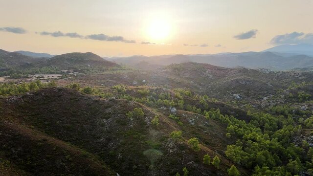 flight over hilly nature reserver with lush green trees during sunset on greece island rhodes