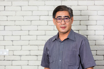 Obraz premium Portrait of Asian handsome senior elderly man wear eyeglasses on white brick wall background. Old man standing golden age grandfather healthcare cheerful lifestyle