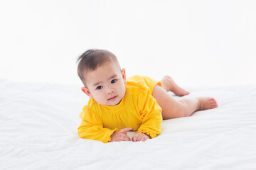 Portrait of beautiful young Asian newborn little baby prone on the bed at home, Happy baby smile wears a yellow shirt relaxing in the room, Family morning at home
