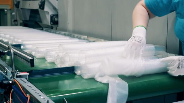 Female worker in gloves packing up plastic cup stacks in plastic bags