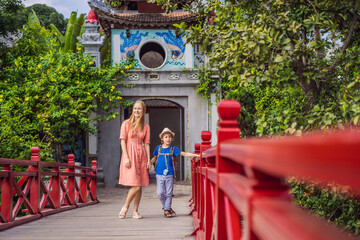 Caucasian mom and son travelers on background of Red Bridge in public park garden with trees and...