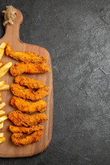 Half shot view of crispy and fried chicken meal on wooden cutting board on dark table