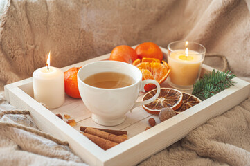 A wooden tray with tea, tangerines, nuts and spices on a beige plaid. Winter breakfast. The concept of hygge.