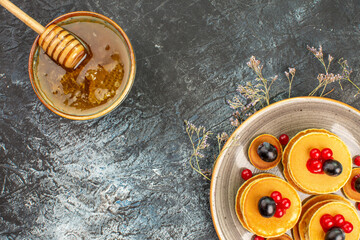 Sweet honey in a brown bowl with wooden spoon and pancakes on gray background