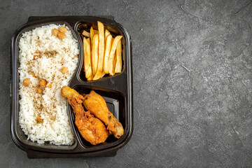 Vertical view of rice and peas meal served with fried chicken and potatoes with on dark table