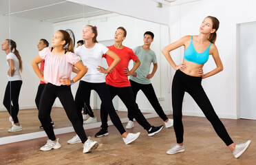 Active group of teenagers participating in dance class, following their young female teacher in dance school