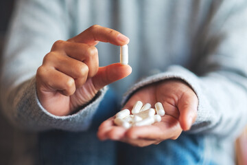 Closeup image of a woman holding and showing white medicine capsules in hand