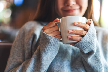 Closeup image of a beautiful young asian woman holding and drinking hot coffee in cafe