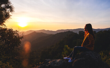 Obraz premium A female traveler sitting on the mountain peak and watching sunrise in the morning