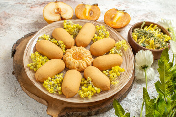 a plate of cookies on wooden platter and a bowl of herb and fruits and flowers on marble ground