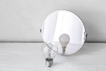 Light bulb looking at its reflection in mirror on white wooden background