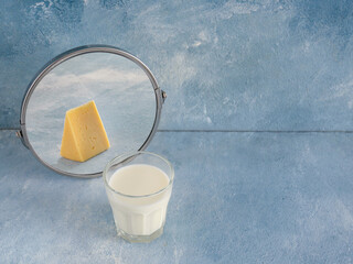 Glass of milk looking at its reflection in mirror on color background