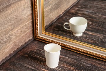 Paper cup looking at its reflection in mirror on wooden background