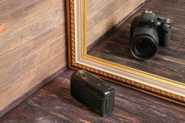 Old photo camera looking at its reflection in mirror on wooden background