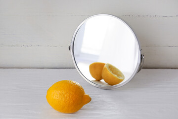 Lemon looking at its reflection in mirror on white wooden background