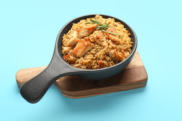Frying pan with tasty pilaf on color background