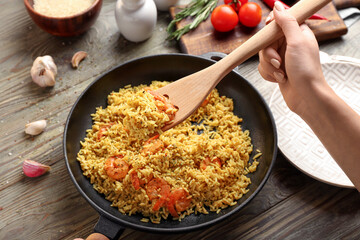 Woman putting pilaf into plate from frying pan on wooden table