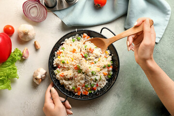Female hands with tasty pilaf and wooden spoon on color background
