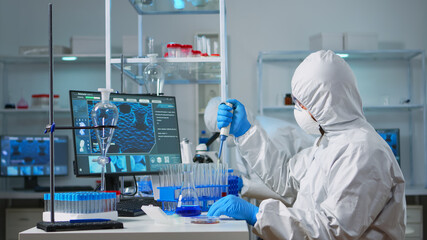 Man scientist in coverall using micropipette in modern equipped laboratory. Team of doctors...