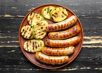 Plate with tasty grilled sausages and vegetables on dark wooden table