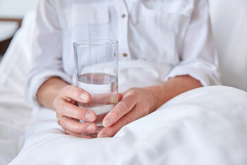 medicine, healthcare and people concept - close up of senior woman with glass of water sitting in bed at hospital ward