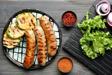 Plate with delicious grilled sausages, vegetables and spices on table