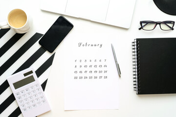 Calendar of February on white desktop flat ley with a cup of coffee and a notebook