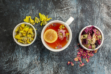 close up view of herbal tea with bowls of dry flowers on grey background