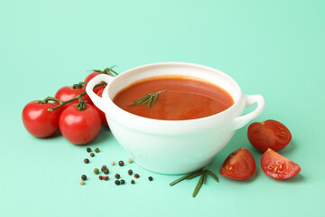 Bowl with tomato soup and ingredients on mint background