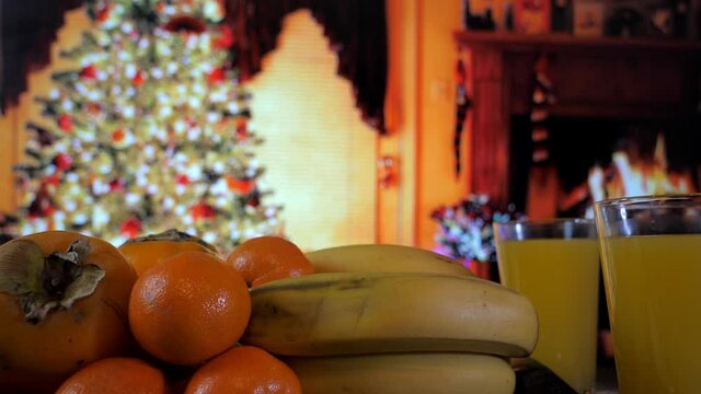 Orange persimmon, a lot of yellow bananas and a glass of juice against the background of a Christmas tree in a cozy room