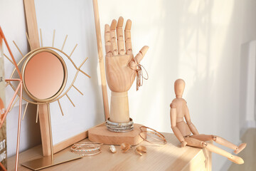 Wooden hand and mannequin with female jewelry on chest of drawers in interior of room
