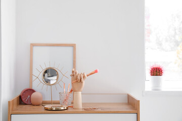 Wooden hand with female jewelry and makeup brushes on table in interior of room