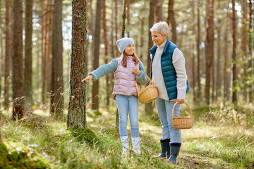 season, leisure and people concept - grandmother and granddaughter with baskets picking mushrooms in forest
