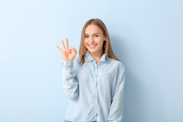 Beautiful young woman showing OK gesture on color background