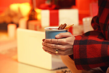 Woman with tasty mulled wine in room decorated for Christmas