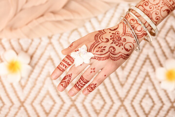 Beautiful female hand with henna tattoo and flower on light background