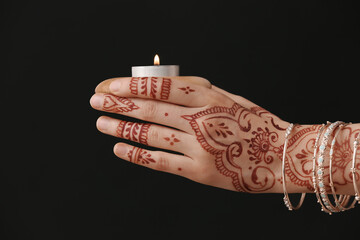 Beautiful female hands with henna tattoo and candle on dark background