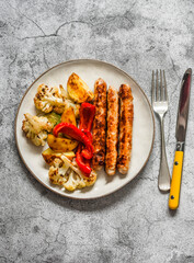 Turkey sausage and baked vegetables on a gray background, top view