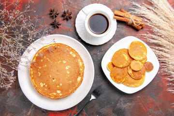 Above view of tasty pancakes on white plates and a cup of tea with cinnamon on mixed color table