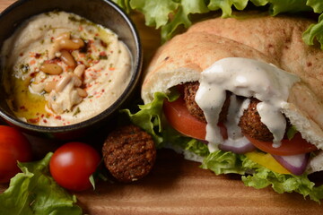 Falafel in pita bread with vegetable salad, harissa sauce, humus, tahini on wooden background. Middle eastern fast food concept. Traditional Israeli food.