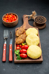 Vertical and close up view of tasty cutlets chopped vegetables greens for dinner on dark background